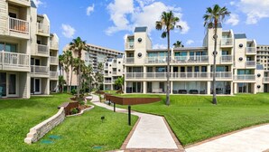 Een hotel met meerdere balkons, een centrale pad en palmbomen.