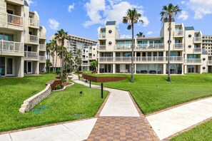 A hotel with multiple balconies, a central pathway, and palm trees. - Solare Seventh Floor Condo (South Padre Island)