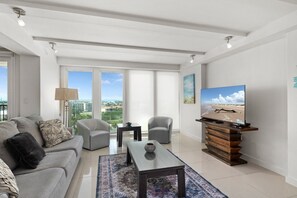 A modern living room with a sofa, two armchairs, a coffee table, a TV on a wooden stand, and large windows with a view. - Solare Seventh Floor Condo (South Padre Island)
