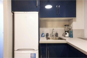 A kitchen with a white refrigerator, dark blue cabinets, a stainless steel sink, a blender, and a kettle. - Spacious, recently renovated apartment near the Louvre (Île-de-France)