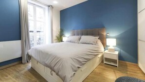 Een slaapkamer met een bed, nachtkastje en uitzicht op een balkon.
