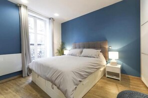 A bedroom with a bed, bedside table, and a view of a balcony. - Spacious, recently renovated apartment near the Louvre (Île-de-France)