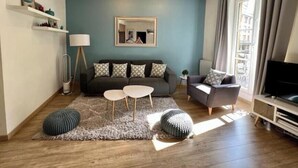 Een moderne woonkamer met een bank, twee bijzettafels, een tv-meubel en een groot raam met gordijnen.