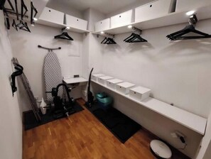 Ein kleines Zimmer mit Holzboden, einer Kleiderstange, einem Staubsauger und Aufbewahrungsboxen auf Regalen.