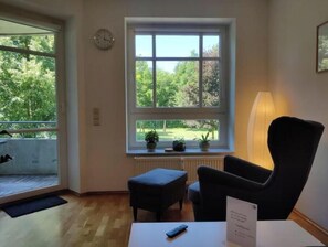 Ein Zimmer mit einem großen Fenster, einem Sessel, einem kleinen Tisch mit Fernbedienung und einer Lampe.