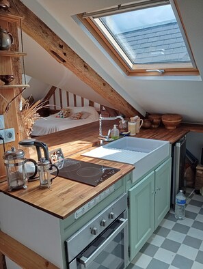 Une cuisine compacte dotée d’une lucarne, de poutres en bois, d’un lit et offrant une vue sur le ciel.