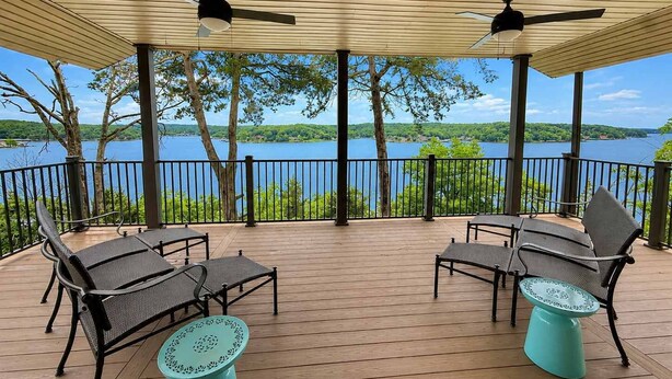 Eine überdachte Terrasse im Freien mit zwei Stühlen und einem Tisch, mit Blick auf einen See.
