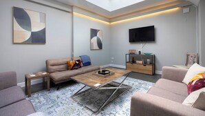Un salon moderne avec un plafond haut, un téléviseur à écran plat et des œuvres d’art abstraites accrochées au mur.