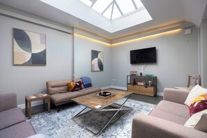 A modern living room with a high ceiling, a flat-screen TV, and abstract wall art. - Spacious Pet Friendly Home in Central Cheltenham. Sleeps 6 FREE Parking! (Cheltenham)