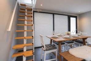 A dining area with a wooden table set for four, a staircase with wooden steps, and a window with blinds. - Spacious Pet Friendly Home in Central Cheltenham. Sleeps 6 FREE Parking! (Cheltenham)