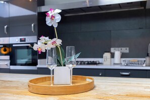 A modern kitchen with a wooden tray holding a white candle and two glasses, and a white orchid in the background. - Spacious Pet Friendly Home in Central Cheltenham. Sleeps 6 FREE Parking! (Cheltenham)