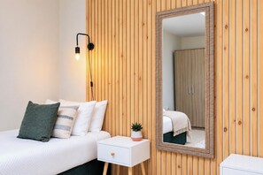 A bedroom with a bed, bedside table, lamp, mirror, and wooden panel wall. - Spacious Pet Friendly Home in Central Cheltenham. Sleeps 6 FREE Parking! (Cheltenham)