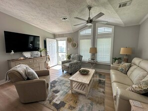 Ein Wohnzimmer mit Fernseher, Deckenventilator, einer Couch, einem Couchtisch und einem gemusterten Teppich.
