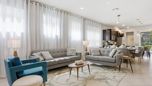 Un salon moderne avec un canapé, des fauteuils, une table basse et un coin cuisine à l’arrière-plan.