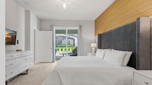 Une chambre moderne avec un grand lit, une tête de lit en bois, une commode blanche et une vue sur un jardin, visible à travers une porte vitrée.