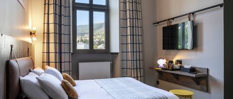 A bedroom with a bed, a ceiling fan, a window with curtains, a bedside table, and a mounted TV.