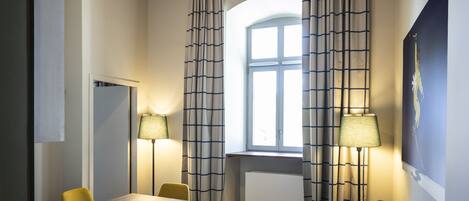 Una habitación con una mesa de comedor, sillas, un sofá, un ventilador de techo y una ventana con cortinas.