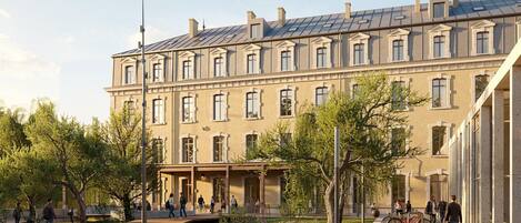 Un immeuble à plusieurs étages, de style architectural classique, doté d’une cour intérieure avec des arbres et d’un petit pont.