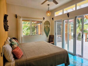 A bedroom with a bed, a ceiling fan, a wall-mounted decorative item, and a view of the outdoors through large sliding glass doors.