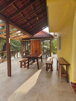 A covered patio area with wooden tables and benches, a wooden pergola, and a yellow wall.