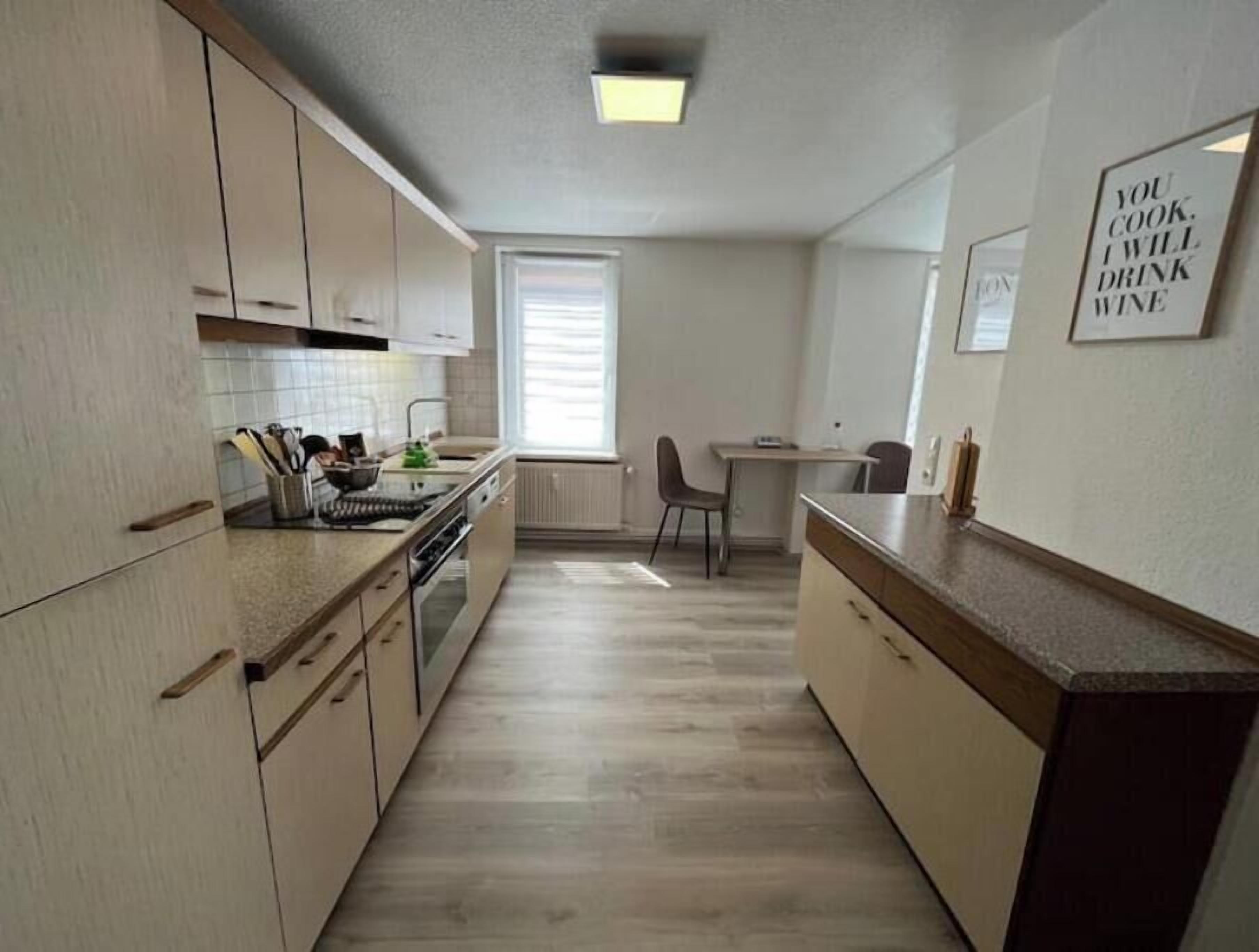 A compact kitchen with wooden cabinets, a dining area with a table and chairs, and a window with blinds.