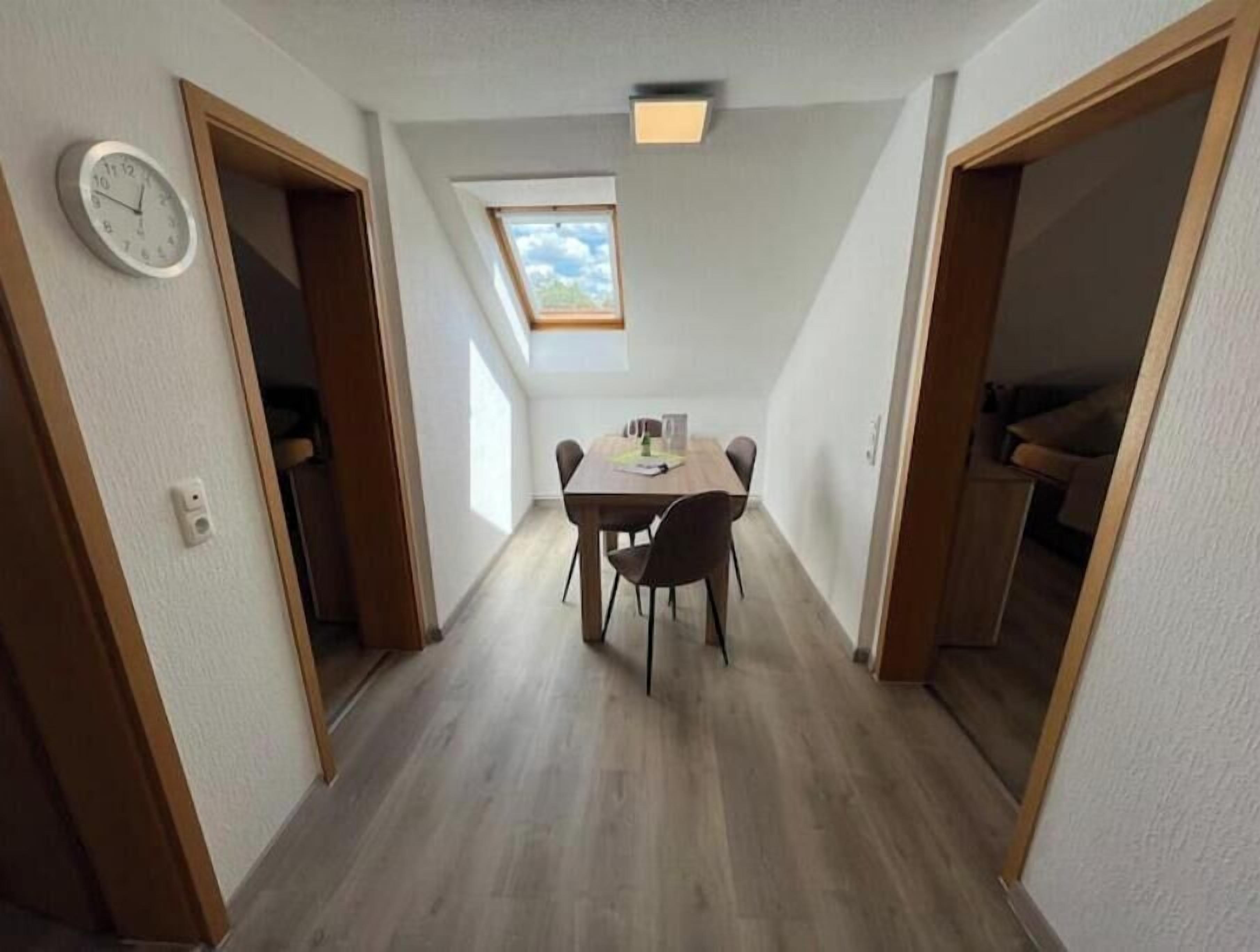 A narrow hallway with a dining table and chairs, a clock on the wall, and a skylight above.