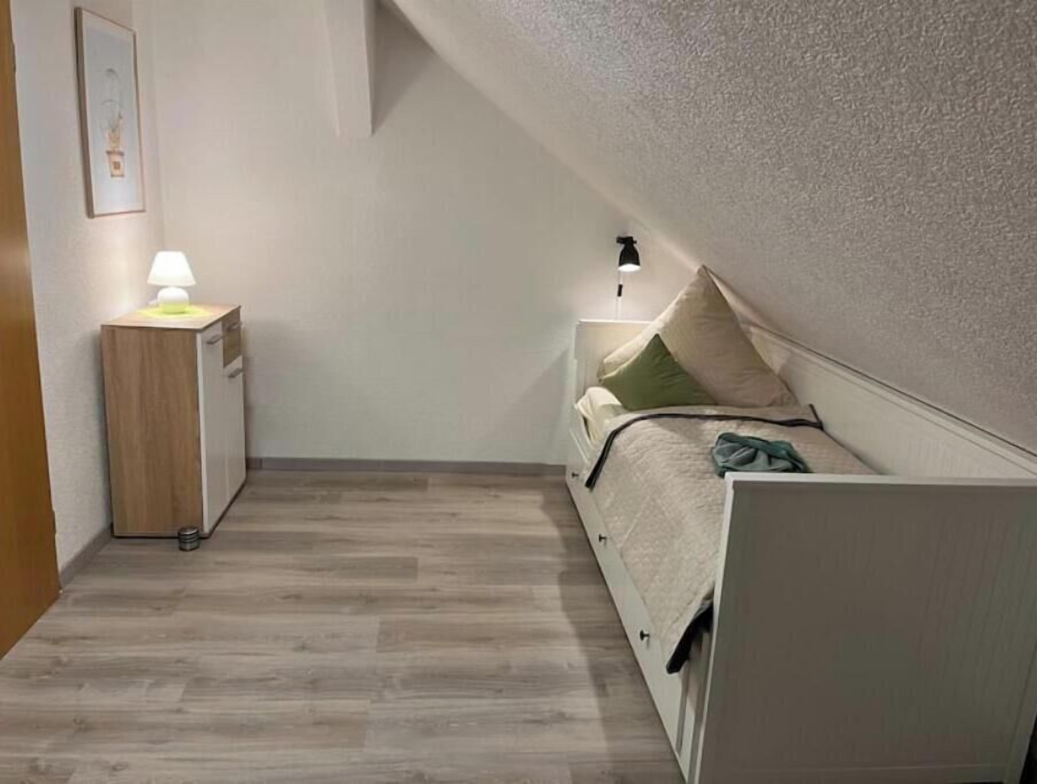 Un dormitorio con cama, mesita de noche, lámpara y un armario pequeño.