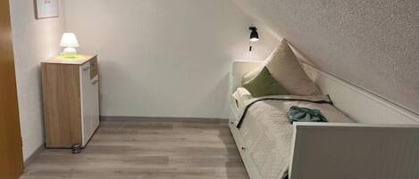 Un dormitorio con cama, mesita de noche, lámpara y un armario pequeño.