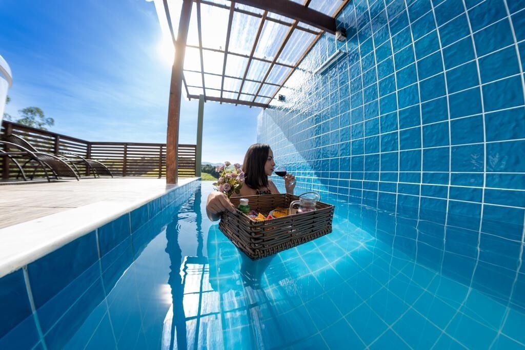 A person relaxing in a swimming pool with a basket of items, surrounded by blue-tiled walls and a pergola structure.