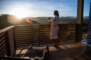 A person standing on a wooden deck with a view of rolling hills, holding a cup and a smartphone.