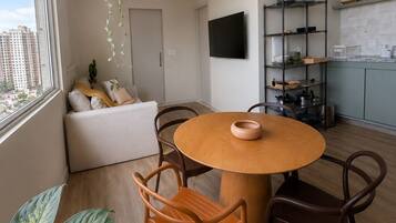 A modern living room with a round wooden table, two chairs, a sofa, and a TV.