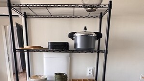A kitchen with a black metal shelving unit holding various kitchenware, a microwave, and a pot on the top shelf.