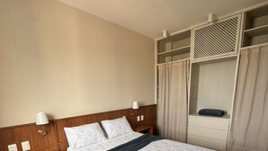 Een keurig opgeruimde hotelkamer met een houten bed, een nachtkastje, een garderobe met spiegel en een plafondlamp.