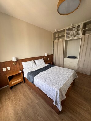 Habitació d'hotel amb llit de fusta, dues taules de nit, un armari amb mirall i una llum al sostre.