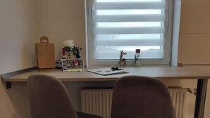 Een kamer met een bureau, twee stoelen, een radiator en een raam met zonwering.