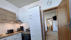 Een kleine keuken met witte kastjes, een fornuis en een koffiezetapparaat.