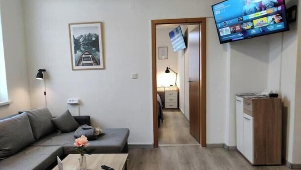 Een moderne woonkamer met een bank, een salontafel met een vaas, een aan de muur bevestigde televisie en een houten kast.