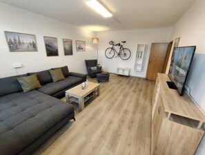 Ein Wohnzimmer mit einer Couch, einem Couchtisch, einem Fernseher und einem an der Wand befestigten Fahrrad.