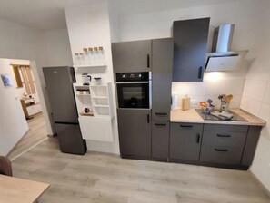 Eine kleine Küche mit Einbauofen, Kühlschrank und Arbeitsplatte mit Küchenutensilien.