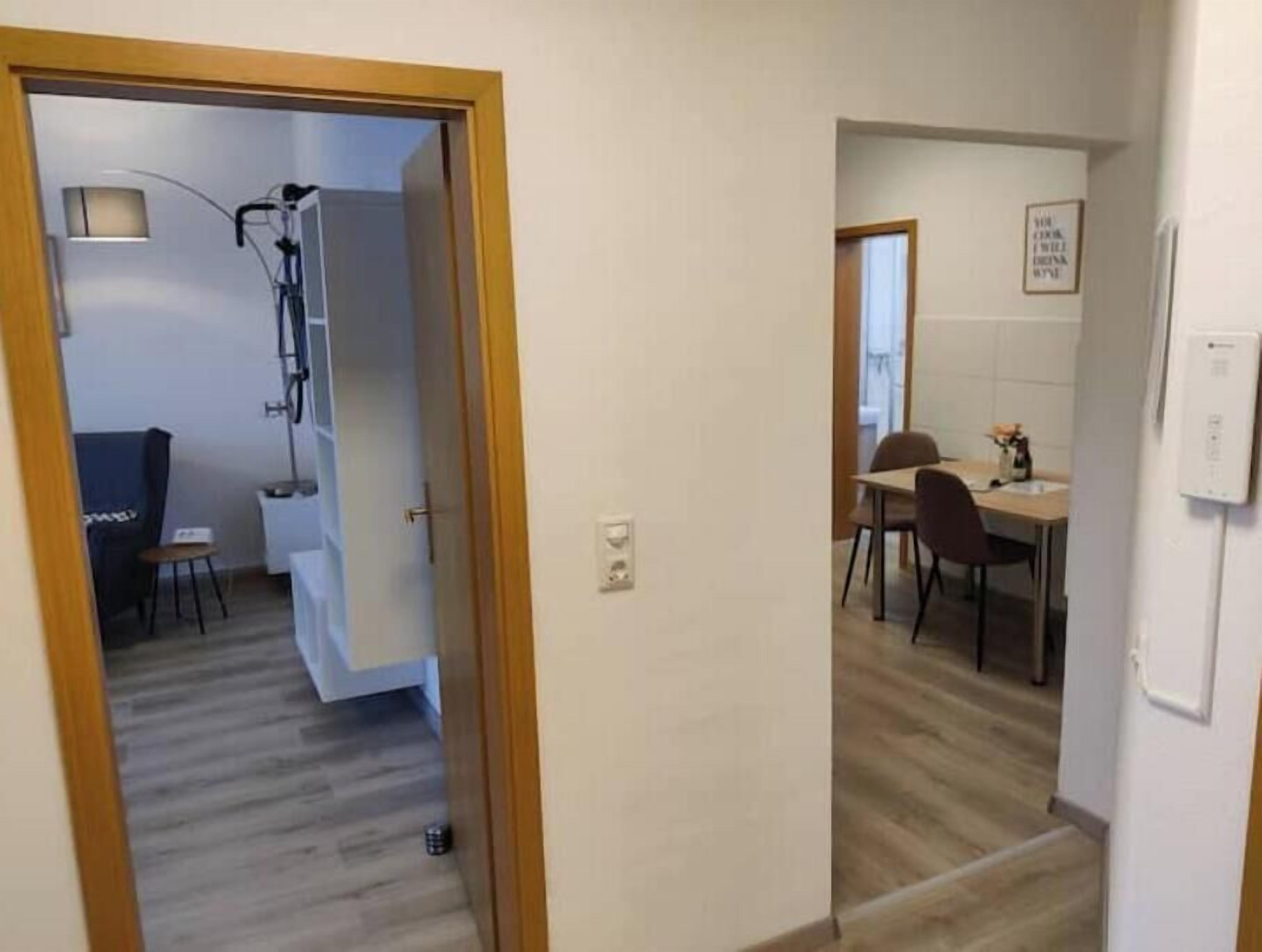 Un couloir mène à une salle à manger équipée d’une table et de chaises, d’un petit tabouret et d’un luminaire fixé au mur.