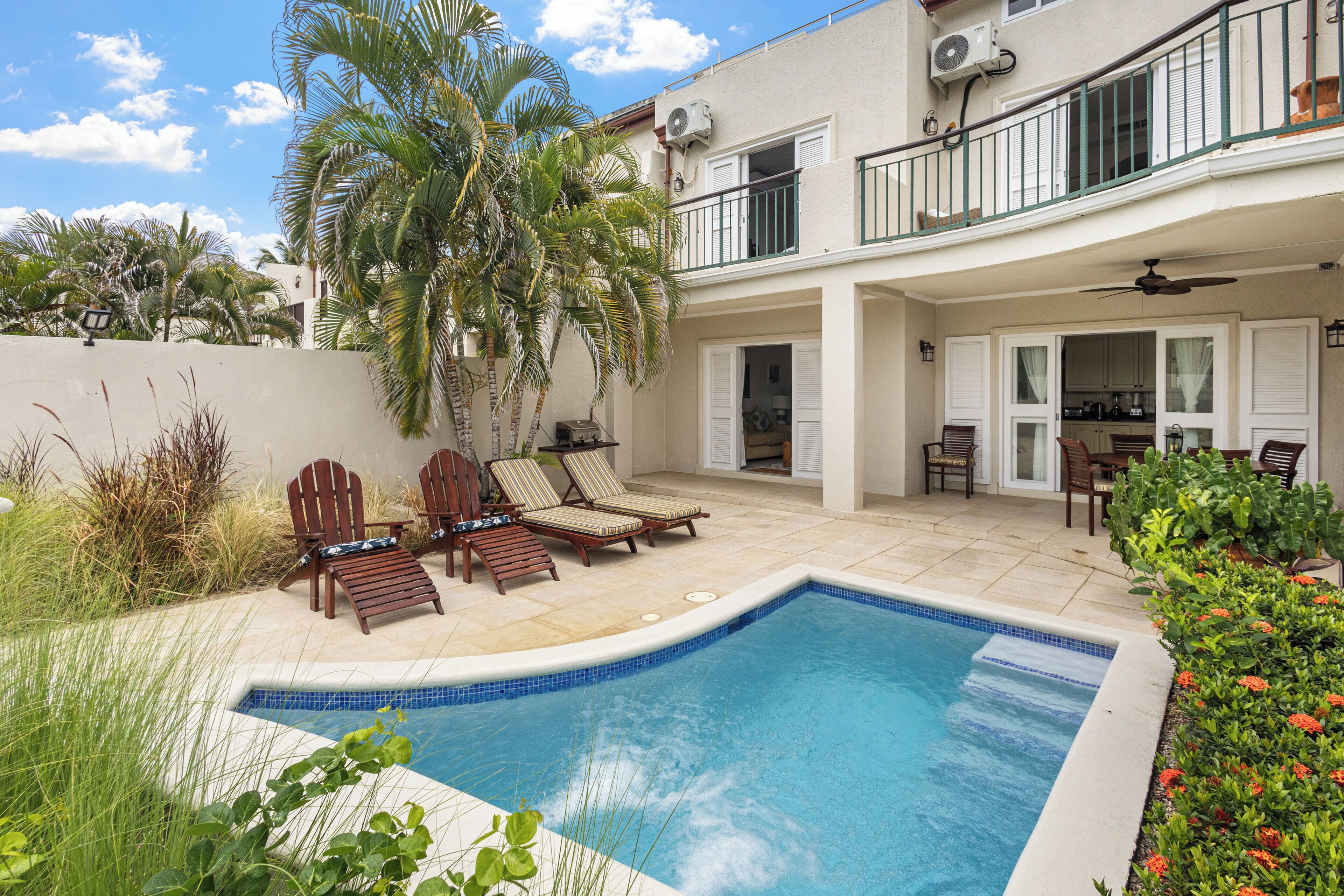A swimming pool with lounge chairs, a balcony with a railing, and a kitchen area with a dining table and chairs.