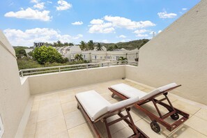 A balcony with two wooden sun loungers and a view of buildings and trees.