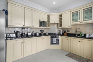 A kitchen with cream-colored cabinets, a black countertop, a microwave, an oven, and various appliances. - Cozy Island-Style Villa - 2 minute walk from beach (Beach)