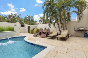 A swimming pool with a water feature, surrounded by lounge chairs and palm trees. - Cozy Island-Style Villa - 2 minute walk from beach (Beach)