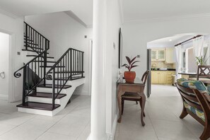 A staircase with black railings, a dining area with a wooden table and chairs, and a kitchen with yellow cabinets. - Cozy Island-Style Villa - 2 minute walk from beach (Beach)
