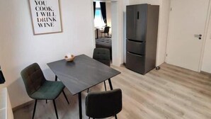 Een klein eethoekje met een tafel, stoelen, een koelkast en een deur.