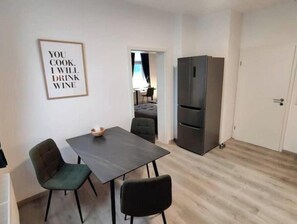 A small dining area with a table and chairs, a refrigerator, and a door. - Feel-good apartment in the heart of Clausthal (Clausthal-Zellerfeld)