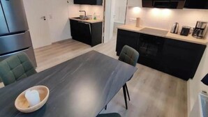 Een compacte keuken met een eethoek, inclusief een koelkast, fornuis, spoelbak en een klein aanrecht met een koffiezetapparaat.