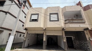 Un edificio de varios pisos con dos puertas de garaje a nivel de calle, un balcón con barandilla decorativa y una ventana pequeña con contraventanas.