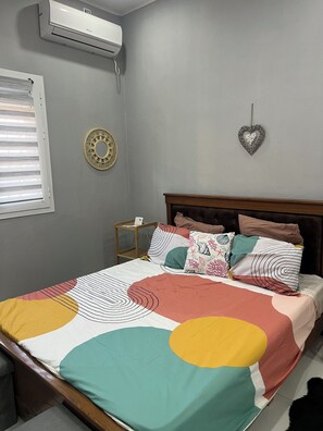 Un dormitorio con cama, aire acondicionado instalado en la pared, un plato decorativo y un adorno con forma de corazón.